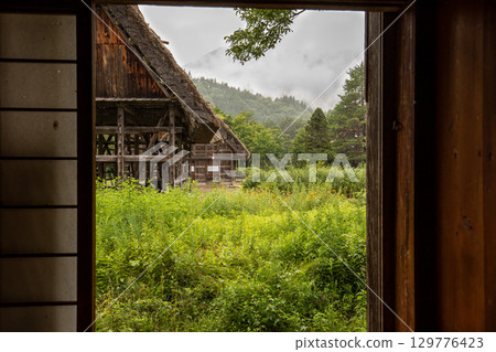 View of Shirakawa-go's old houses and mountains from inside the house in the rain View of Shirakawa-go's old houses and mountains from inside the house in the rain 129776423