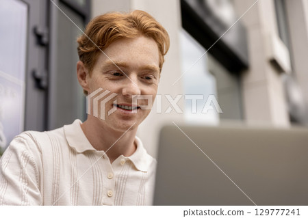 Young freelancer working on laptop sitting in street cafe using internet 129777241