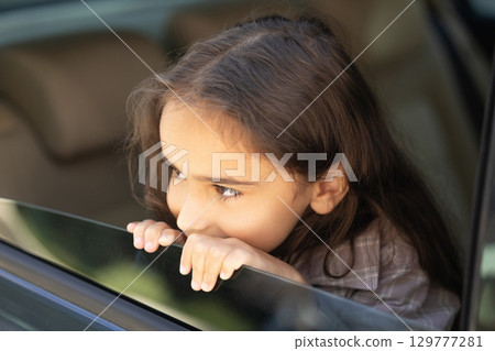 Headshot of a cute school-aged girl looking out of the car window 129777281