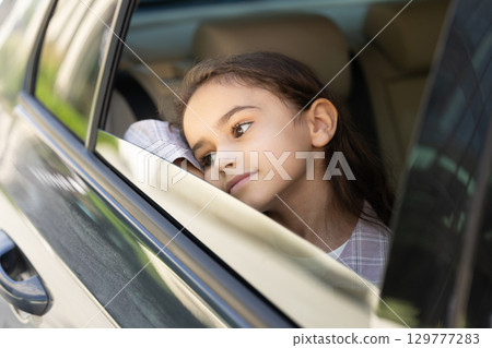 Headshot of a cute school-aged girl looking out of the car window 129777283