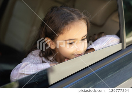 Headshot of a cute school-aged girl looking out of the car window 129777294