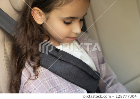 Cute school-aged girl sitting in a car with her seatbelt fixed 129777304