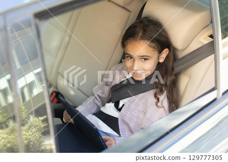 Cute school-aged girl sitting in a car with her seatbelt fixed 129777305