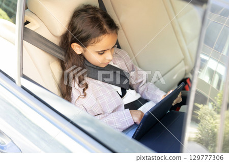 Cute school-aged girl sitting in a car with her seatbelt fixed 129777306