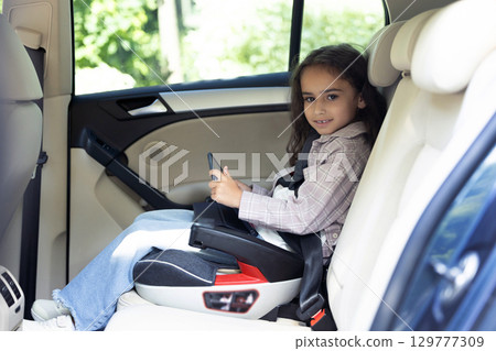Cute school-aged girl sitting in a car with her seatbelt fixed 129777309