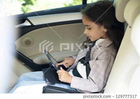 Dark-haired girl of school age sitting in a care with her seatbelt fixed 129777317