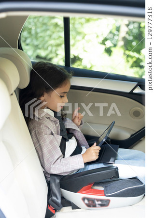 Dark-haired girl of school age sitting in a care with her seatbelt fixed 129777318