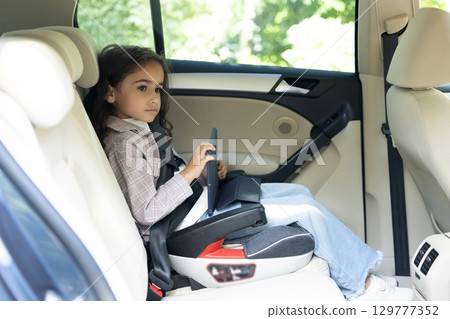 Dark-haired girl of school age sitting in a care with her seatbelt fixed Dark-haired girl of school age sitting in a care with her seatbelt fixed 129777352