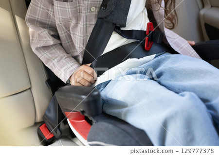 Close up of a kid in a car fixing a seatbelt 129777378