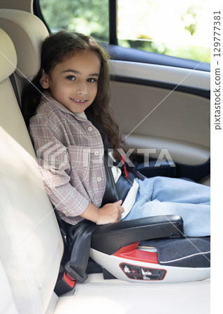 Dark-haired girl of school age sitting in a care with her seatbelt fixed 129777381