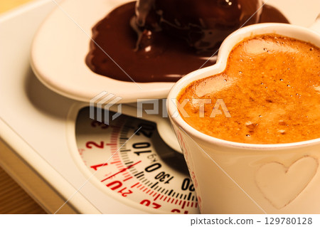 Coffee and chocolate cake on weighing scale. 129780128