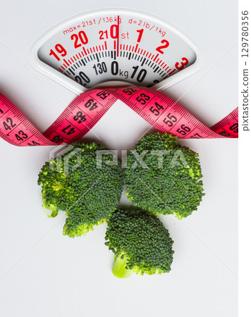 Broccoli with measuring tape on weight scale. Dieting Broccoli with measuring tape on weight scale. Dieting 129780356