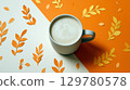 Cup of frothy coffee on orange and cream background with autumn-themed paper cut leaves 129780578