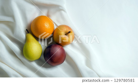 Fresh fruits including pear, orange, apple, and plum arranged on soft white fabric in natural light 129780581