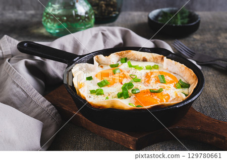 Homemade scrambled eggs in pita bread with herbs in a frying pan on the table 129780661