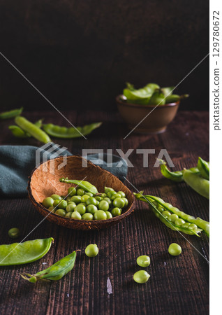 Fresh green peas in a bowl and in pods on the table vertical view 129780672