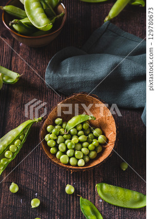 Bowl with green sugar peas on wooden table vertical view 129780673