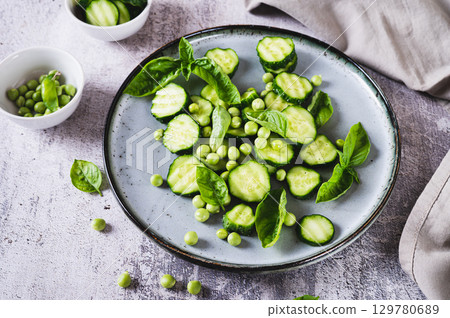 Green vegetarian salad with cucumbers, peas and basil on a plate on the table Green vegetarian salad with cucumbers, peas and basil on a plate on the table 129780689