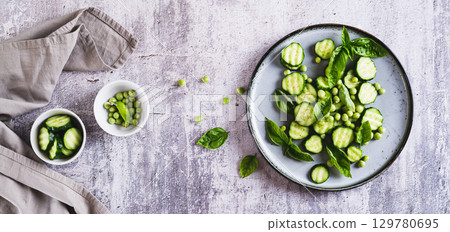 Green vegetarian salad with cucumbers, peas and basil on a plate top view web banner 129780695