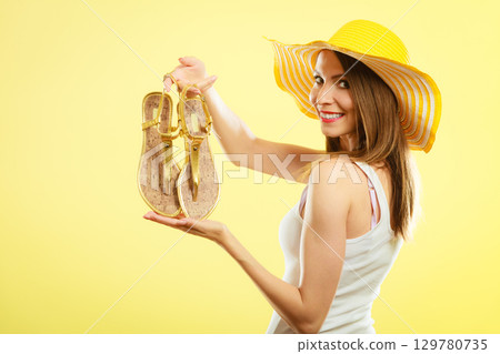 Woman in big yellow summer hat holds sandals Woman in big yellow summer hat holds sandals 129780735