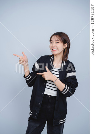 Cheerful young woman points with both hands against a plain gray background, dressed in casual black and white clothing with a friendly smile. Cheerful young woman points with both hands against a plain gray background, dressed in casual black and white clothing with a friendly smile. 129781197