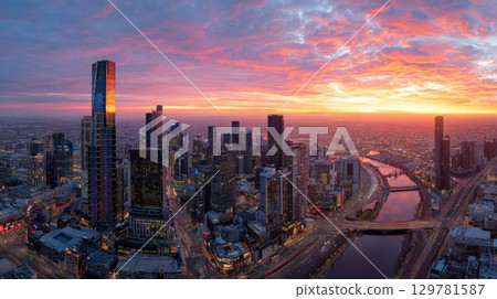 Panoramic sunrise over the sprawling Melbourne city skyline, with skyscrapers and the Yarra River bathed in vibrant golden light 129781587