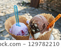 Two ice cream cones held outdoors on a sunny day 129782210