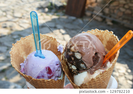 Two ice cream cones held outdoors on a sunny day 129782210