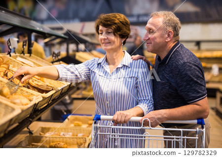 Mature family of retirees examines bread and pastries in grocery section of a supermarket Mature family of retirees examines bread and pastries in grocery section of a supermarket 129782329