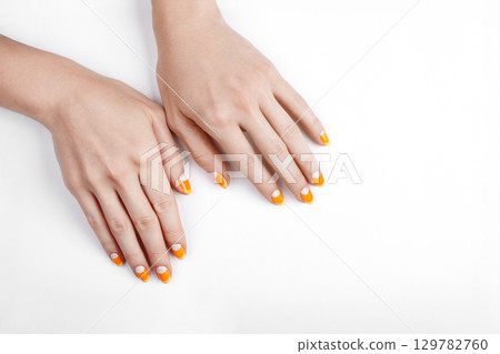 Close-up of female hands with bright orange manicure like candy corn. Creative gel nail design on white background. Halloween nail art, fashion beauty and stylish manicure concept. Halloween Style Close-up of female hands with bright orange manicure like candy corn. Creative gel nail design on white background. Halloween nail art, fashion beauty and stylish manicure concept. Halloween Style 129782760