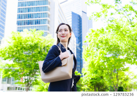 一位女商務人士漫步在綠樹成蔭的城市 129783236