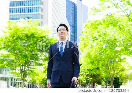 Male business person walking through the green city 129783254