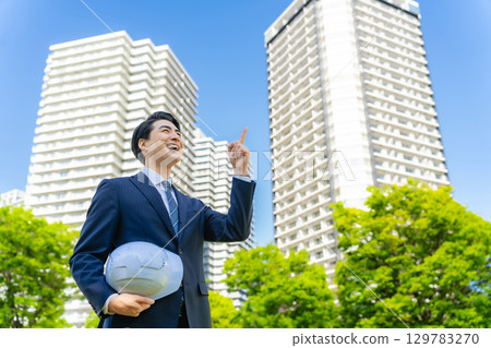 Male business person pointing at the sky in front of a building 129783270