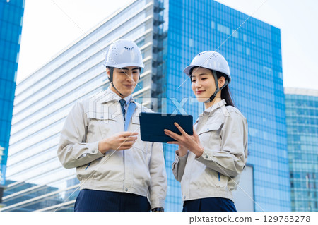 A group of male and female engineers having a meeting while looking at a tablet at a construction site 129783278