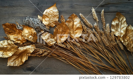 Golden fall leaves and dried wheat arranged artistically on a rustic wooden table . 129783802