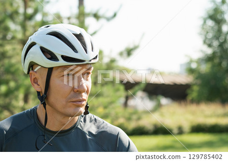 Portrait of cyclist in white helmet at city public park. Summer outdoor activities. 129785402