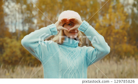 Portrait of happy young woman showing heart shaped sign gesture with hands in autumn park 129785826