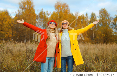 Happy cheerful young two women friends in autumn park, stylish girlfriends smiling together outdoors Happy cheerful young two women friends in autumn park, stylish girlfriends smiling together outdoors 129786057