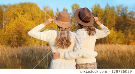 Two women friends together in autumn park, stylish girlfriends in hat, trees with yellow leaves Two women friends together in autumn park, stylish girlfriends in hat, trees with yellow leaves 129786059