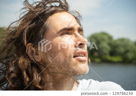 Happy brunette man enjoy and looking to sun at urban park. Enjoying nature and sunny day. Summer. Reflection and wanderlust. Breathe in clean air 129786230