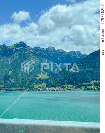 Stunning view of majestic mountains towering over a tranquil turquoise lake under a vibrant blue sky with scattered clouds. A picturesque landscape perfect for travel and nature enthusiasts. Stunning view of majestic mountains towering over a tranquil turquoise lake under a vibrant blue sky with scattered clouds. A picturesque landscape perfect for travel and nature enthusiasts. 129786297