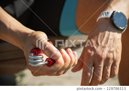 Man strengthens his grip using hand red metal expander. He is seen holding expander with firm grip, suggesting focused exercise 129786313