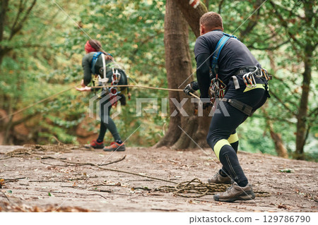 Setting up the ropes. Man and woman doing climbing in forest with use of safety equipment 129786790