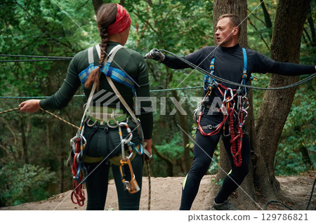 In the forest. Man and woman doing climbing with use of safety equipment In the forest. Man and woman doing climbing with use of safety equipment 129786821
