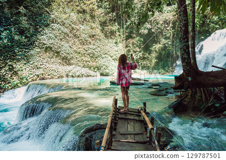 Woman with smartphone on scenic cascade waterfalls with turquoise water 129787501