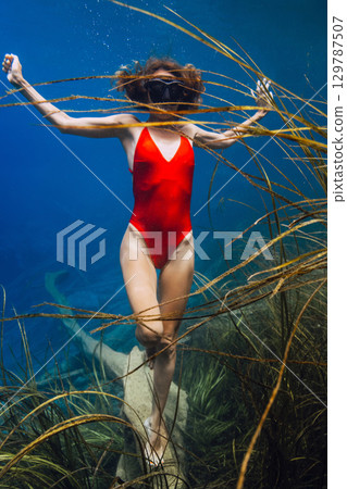 Slim woman underwater swims in blue lake with algae. Slim woman underwater swims in blue lake with algae. 129787507