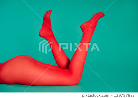 Long legs of beautiful young woman in bright red tights relax on green background Long legs of beautiful young woman in bright red tights relax on green background 129787652