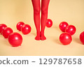 Female legs in red tights among red balloons on beige background 129787658