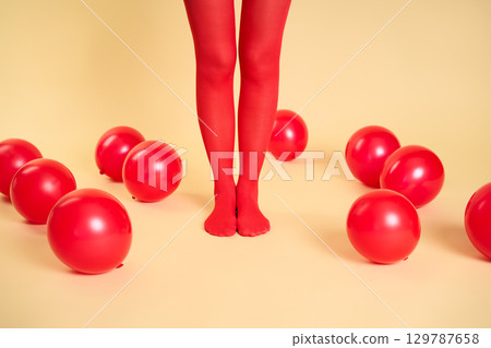Female legs in red tights among red balloons on beige background 129787658