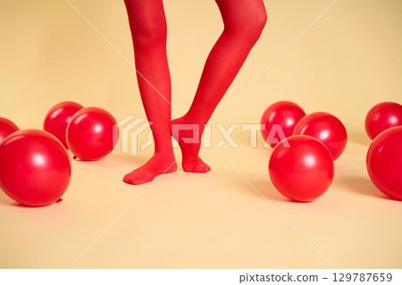 Female legs in red tights among red balloons on beige background 129787659
